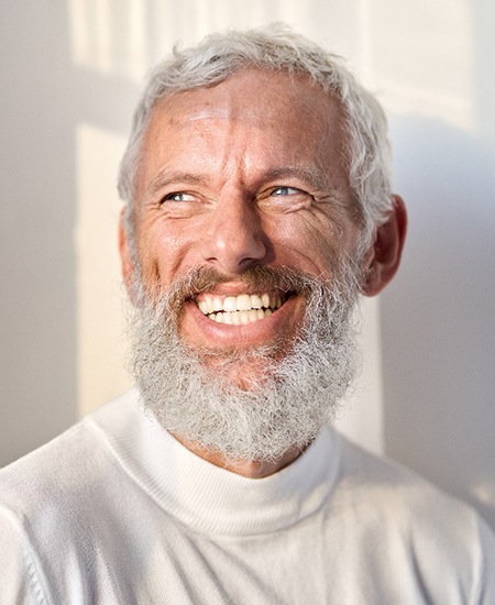 Senior man in white shirt smiling against wall