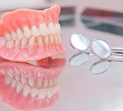 Close-up of full dentures in Indianapolis, IN next to dental mirror