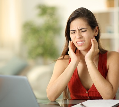 Grimacing woman sitting at computer, dealing with TMD symptoms