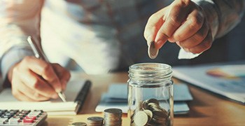 Man dropping coins into a mason jar on his desk